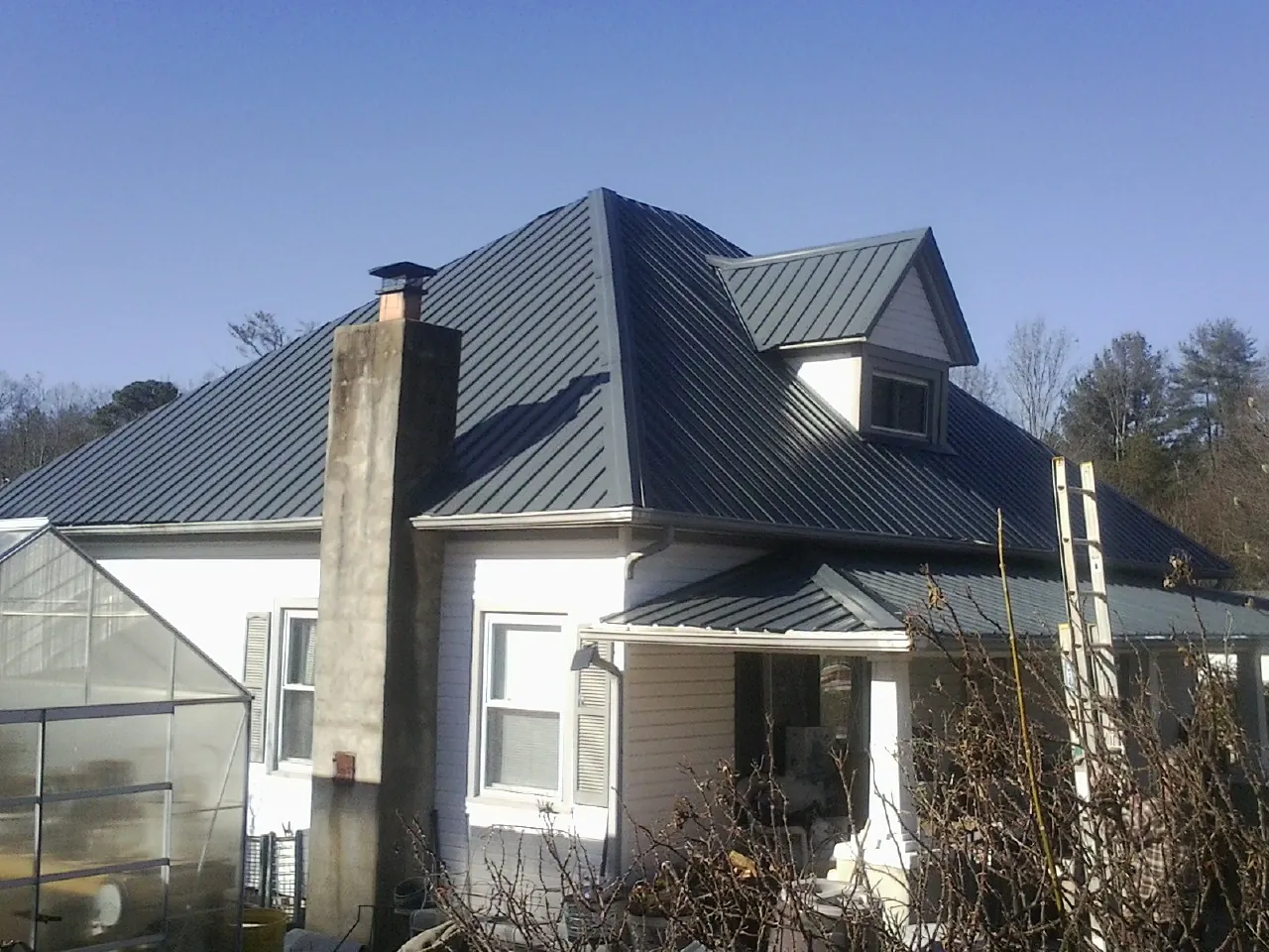 Dark blue standing seam metal roof on a white farmhouse with dormer — Slate & Tile Roof Repair by Roofing Brothers in Ronkonkoma