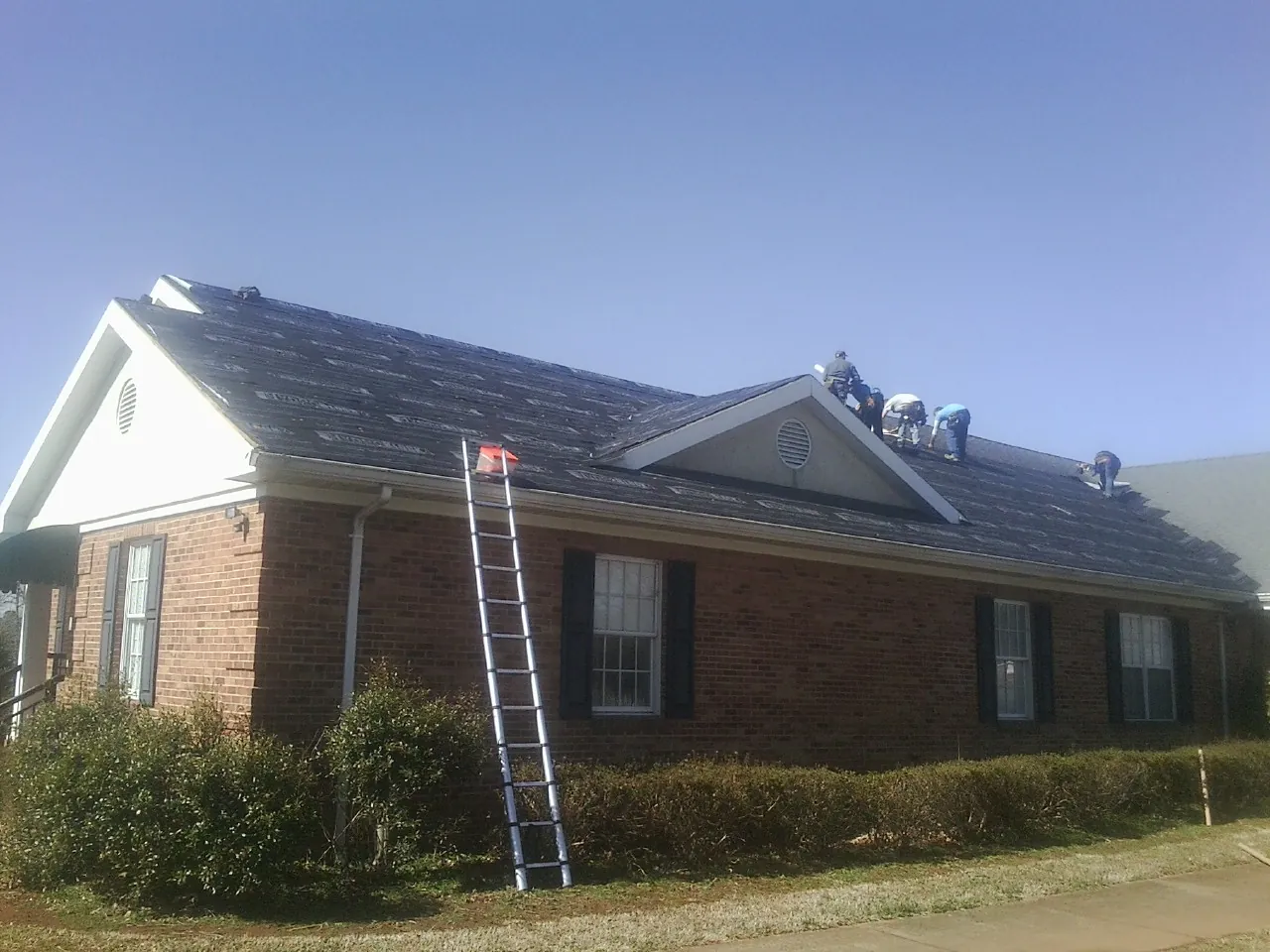 Crew tearing shingles off a brick ranch roof with a ladder set — Metal Roof Repair work by our crew in Ronkonkoma