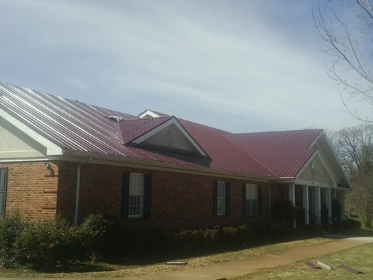 Red metal roof with gabled entries on a long brick building, from a Hail Damage Roof Repair job in Ronkonkoma