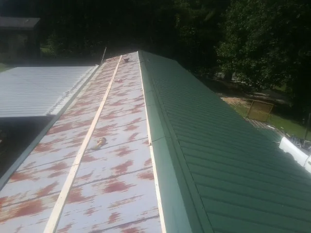 Old rusted panels beside newly installed green metal roofing — Wind Damage Roof Repair by Roofing Brothers in Ronkonkoma