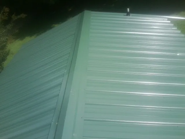 New green metal panels meeting at the ridge of a roof — Flat Roof Repair work by our crew in Ronkonkoma
