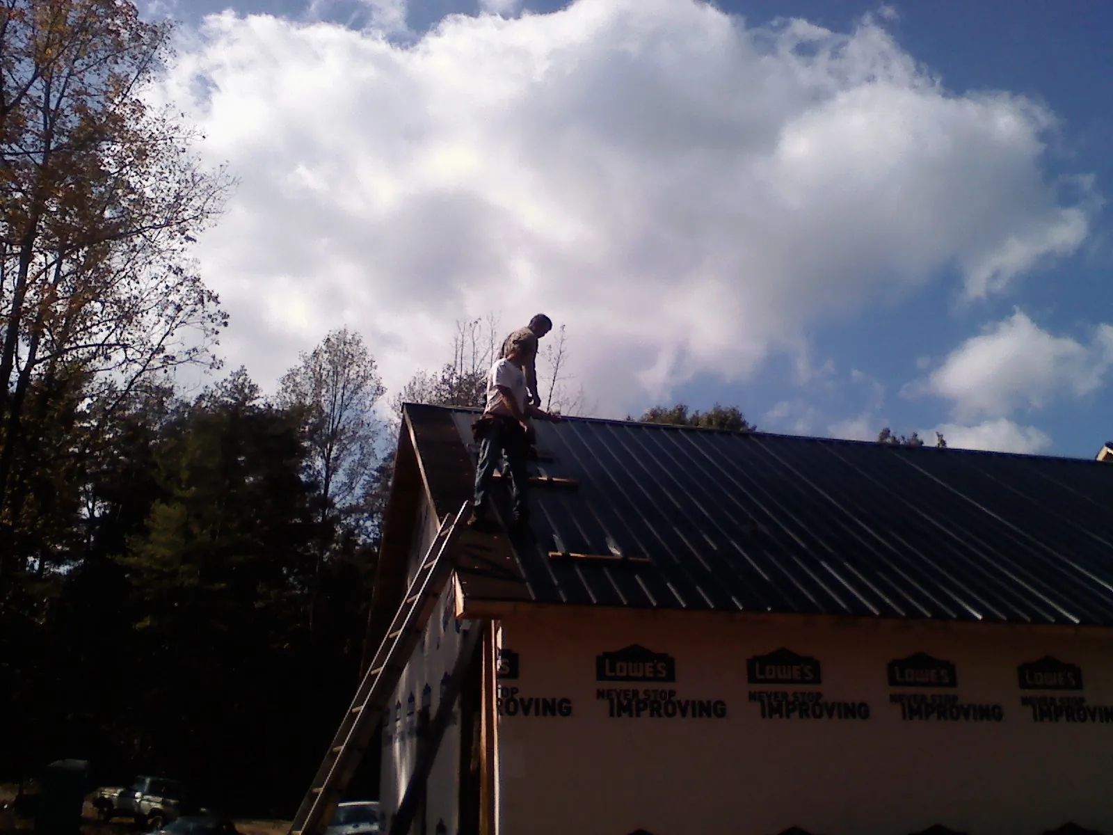 Roofer fastening dark metal panels high against a cloudy sky, from a Roof Inspection job in Ronkonkoma