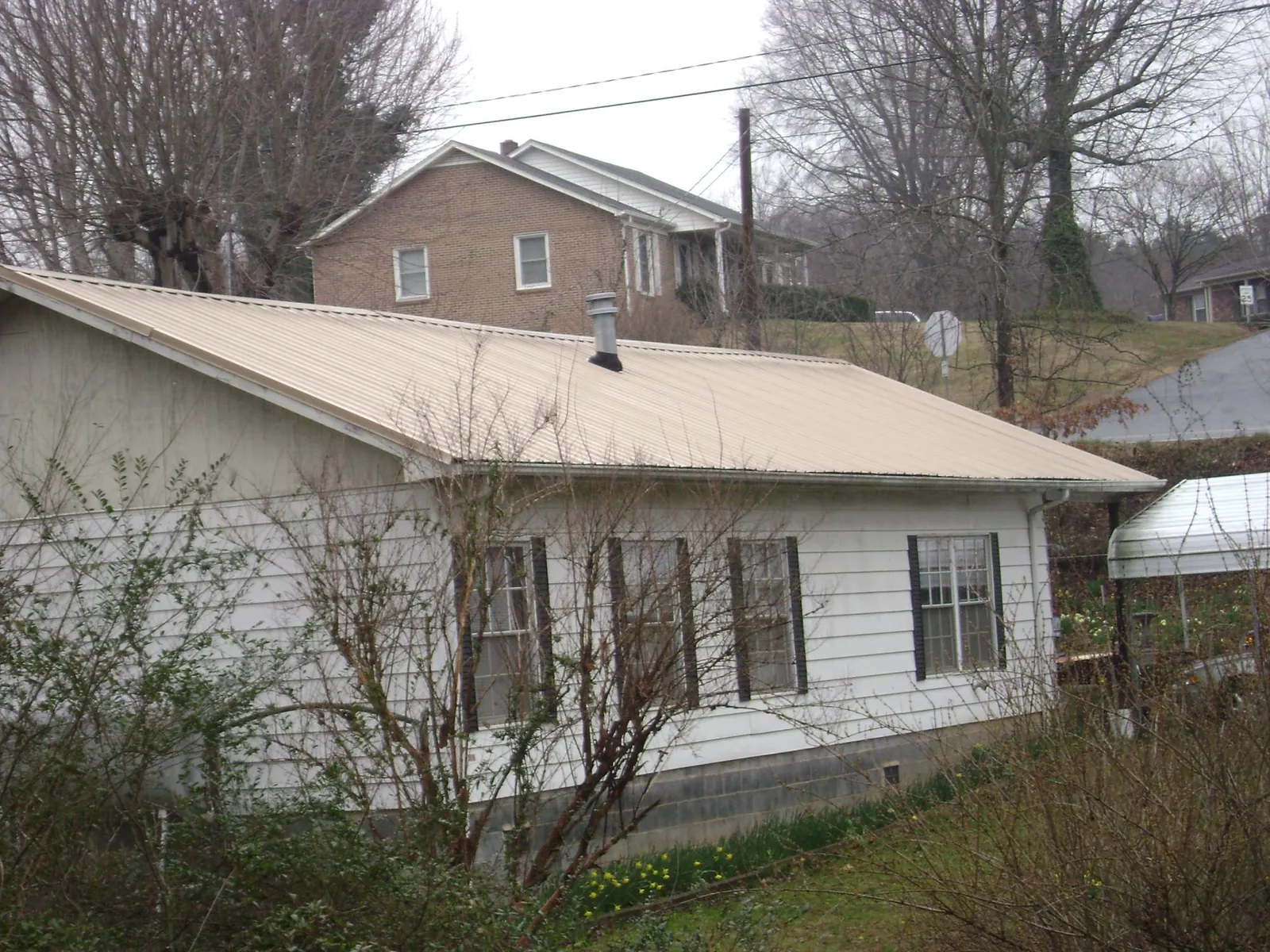 Tan metal roof on a white sided house set into a hillside — Commercial Roofing by Roofing Brothers in Ronkonkoma